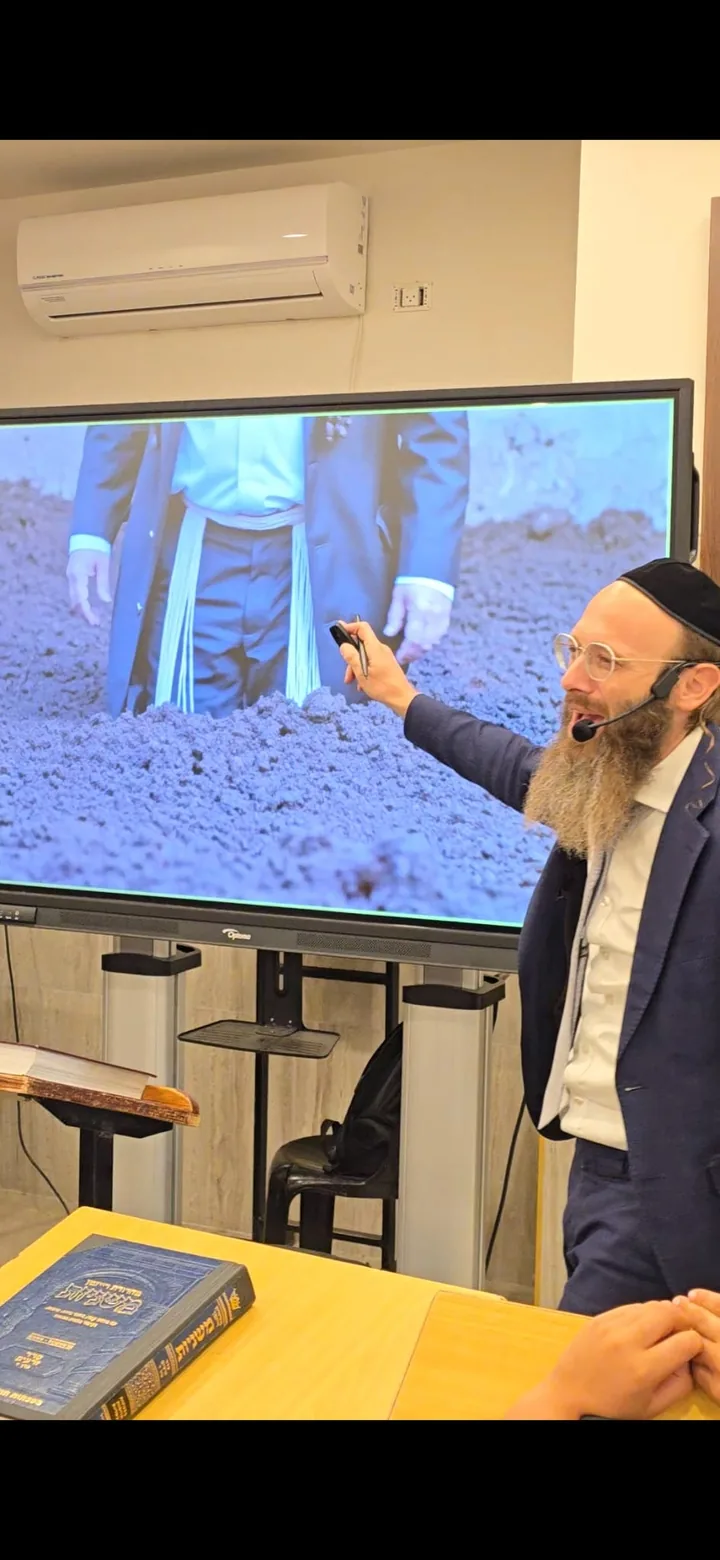 Rabbi Scheller teaching beside a large classroom display with Mishnayos sefarim on the table